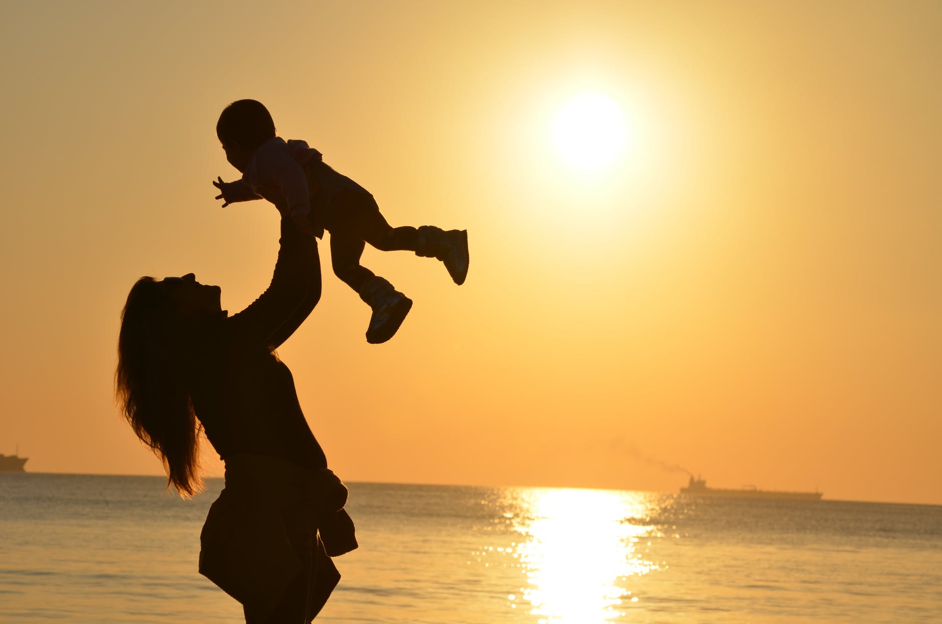 silhouette photo of a mother carrying her baby at beach during golden hour